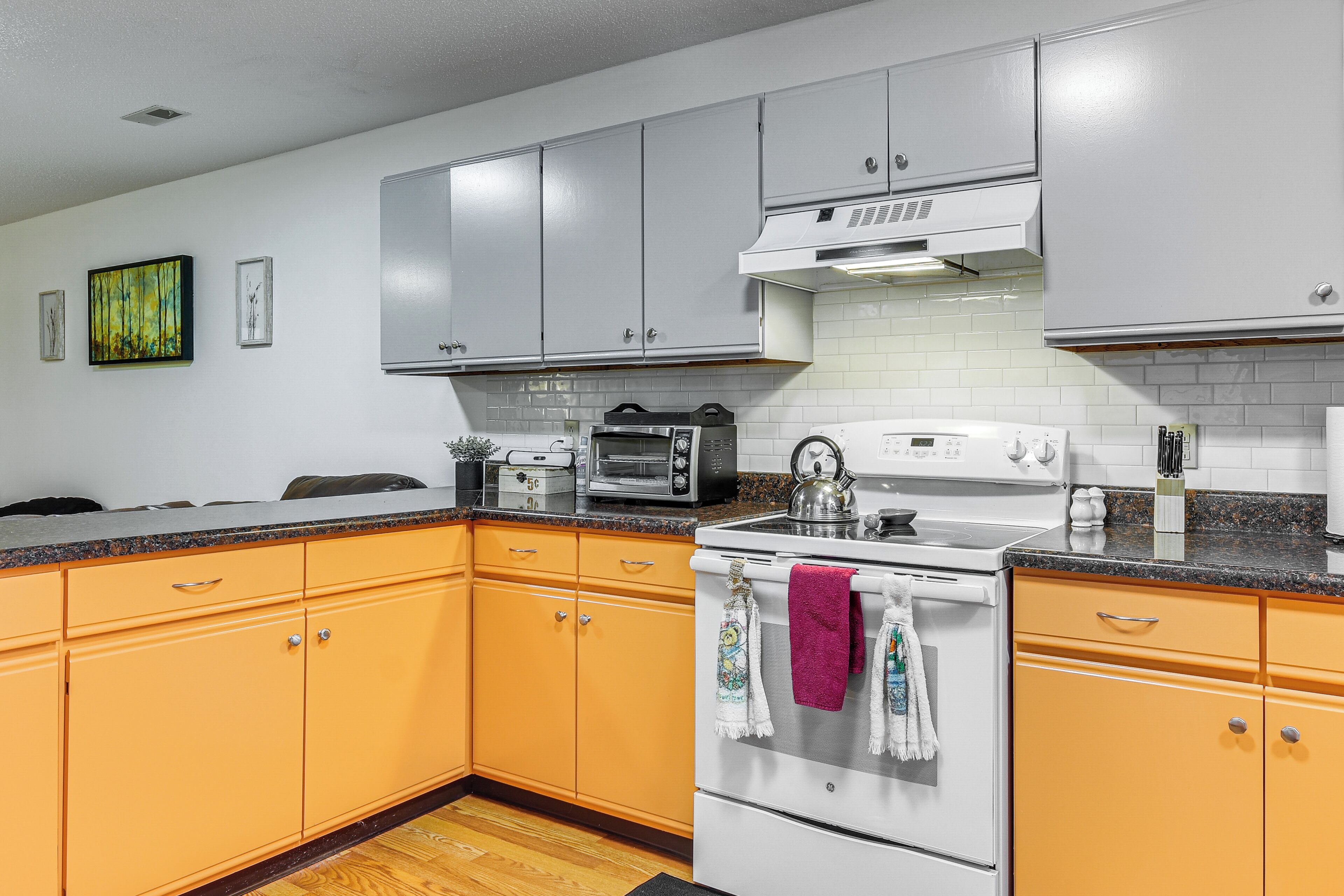 A kitchen with white and orange cabinets, a microwave, a stove, and a toaster.