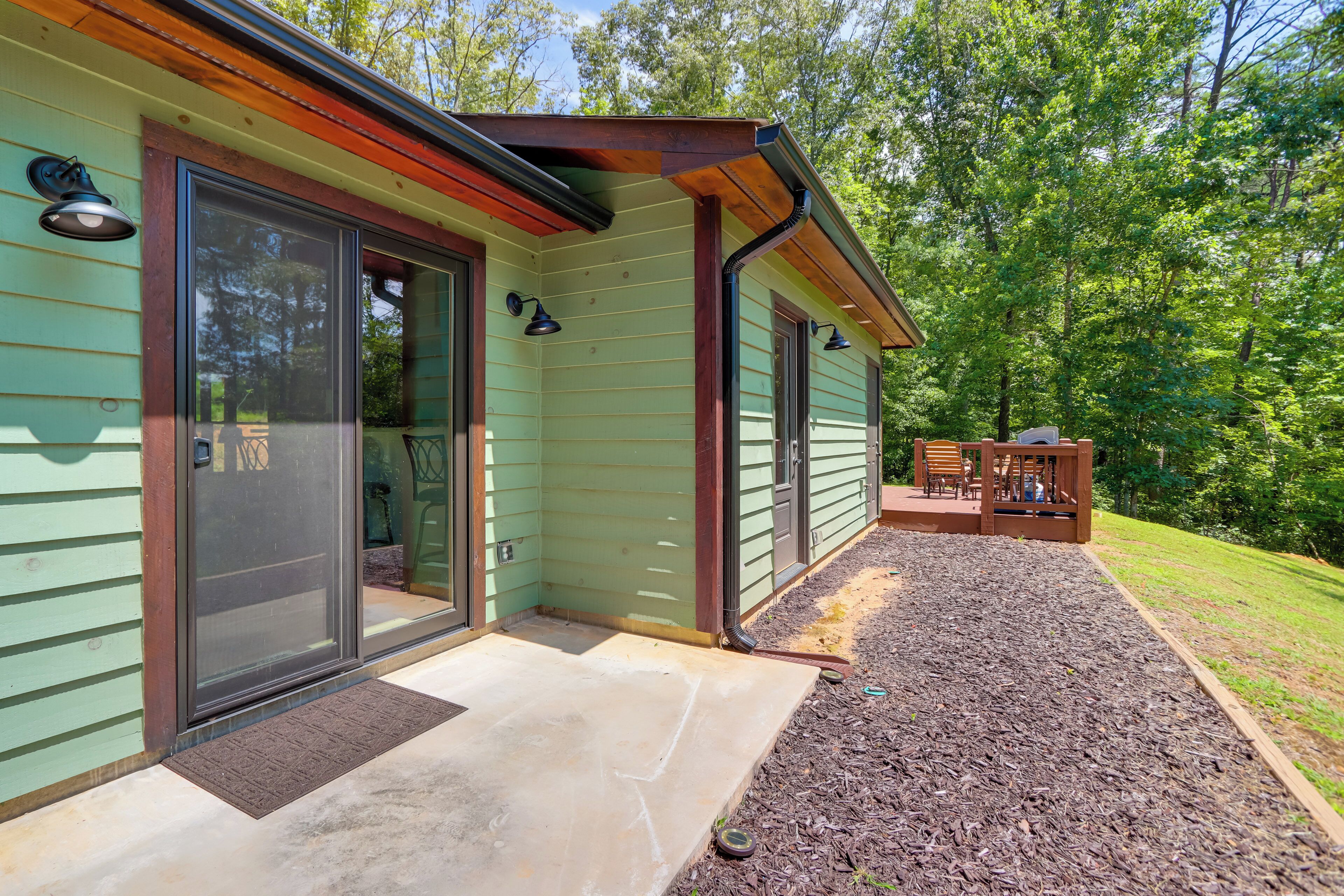 A house with a green exterior, a covered porch with chairs, and a wooden deck.