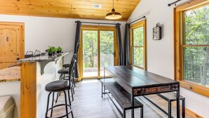 Eine Holzbalkendecke, ein Esstisch mit Stühlen, eine Bar und große Fenster mit Vorhängen.