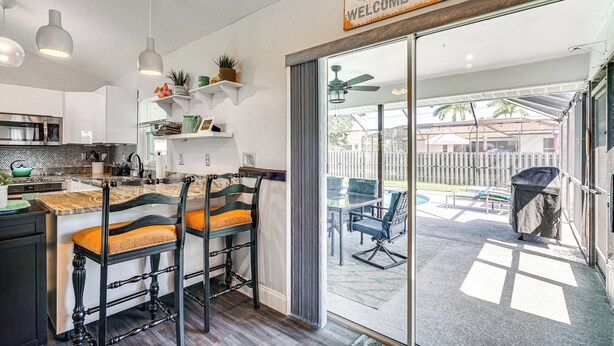 A modern kitchen with a bar area, a sliding glass door leading to an outdoor patio, and a 'Welcome Here' sign.