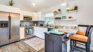 A modern kitchen with stainless steel appliances, white cabinetry, and a wooden floor.