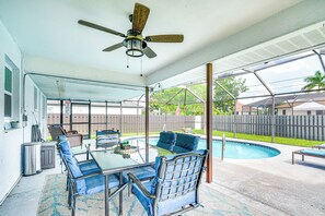A covered patio with a glass table, blue chairs, a ceiling fan, and a pool in the background. - Private Pool & Yard: Dog-friendly Cape Coral Home (Cape Coral)
