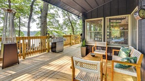 Een overdekt terras met houten meubels, een barbecue en uitzicht op de omliggende bomen.
