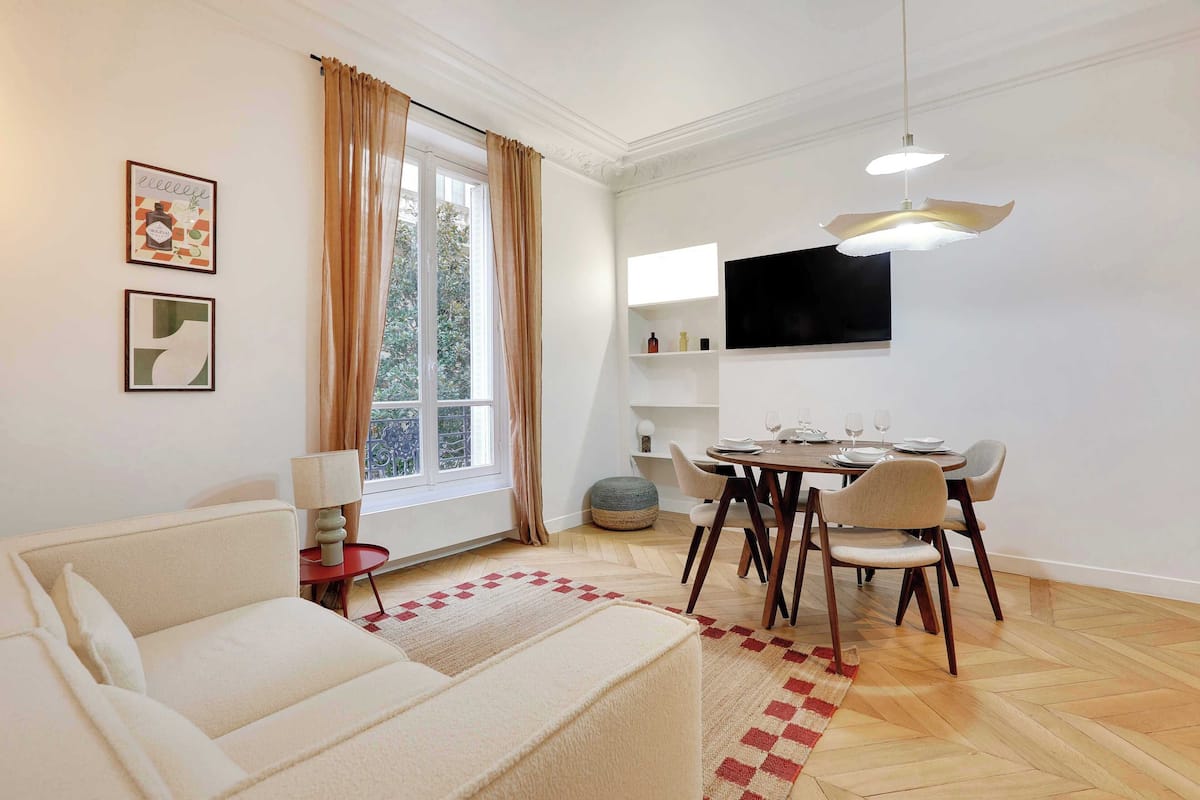 Ein modernes Wohnzimmer mit einer Couch, einem Esstisch, Stühlen und einem an der Wand befestigten Fernseher.