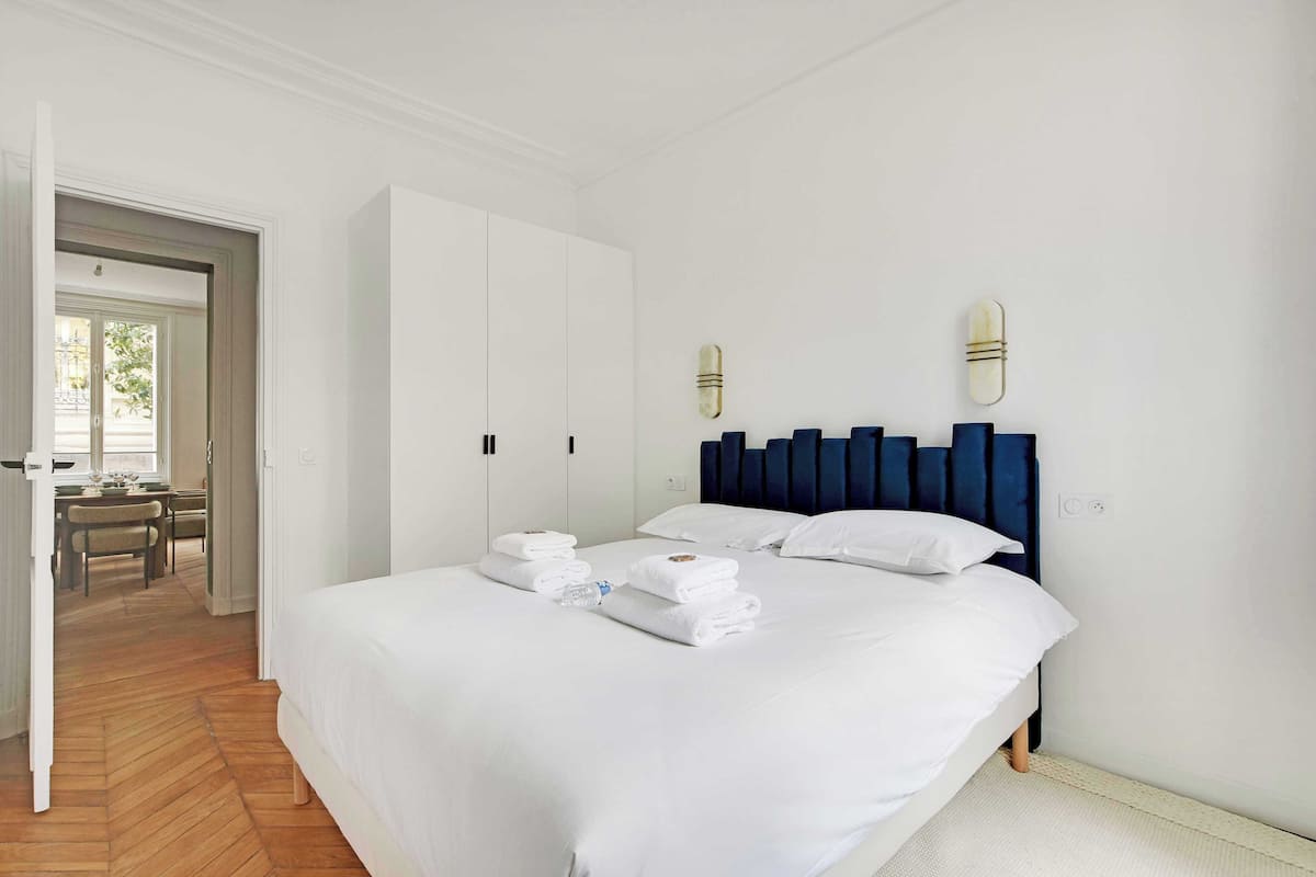 Ein Hotelzimmer mit einem großen Bett, weißen Wänden, einem Holzboden und einer Tür, die auf einen Balkon führt.