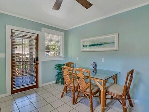 A dining area with a glass table and wooden chairs, a ceiling fan, and a door with metal bars. - Picturesque Bungalow in Savannah (Savannah)