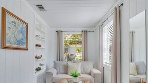 Una habitación con sofá, una mesita de vidrio, una planta en maceta y estanterías con adornos.