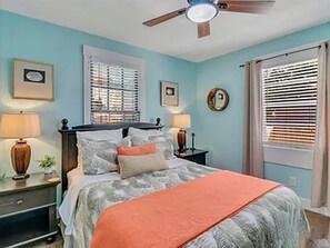 A bedroom with a bed, two bedside tables, a ceiling fan, and a window with blinds. - Picturesque Bungalow in Savannah (Savannah)