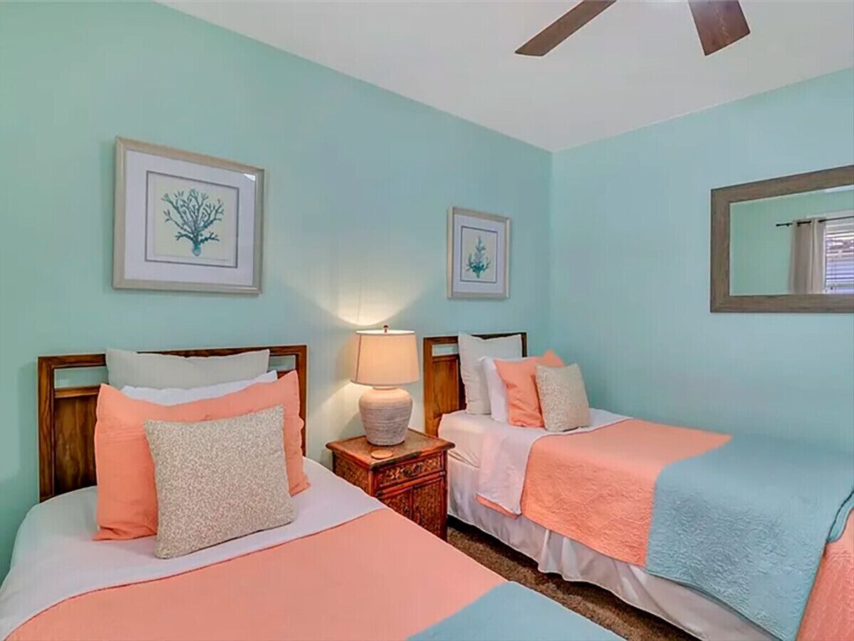 Une chambre avec deux lits, une table de chevet avec une lampe et des œuvres d’art encadrées accrochées aux murs.