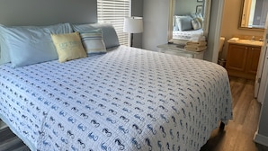 A bedroom with a large bed, a bedside table with a lamp, a mirror, and a view of a bathroom. - Luna Bungalow | New Orleans Soul Meets Gulf Coast Charm in Historic Pensacola (Pensacola)