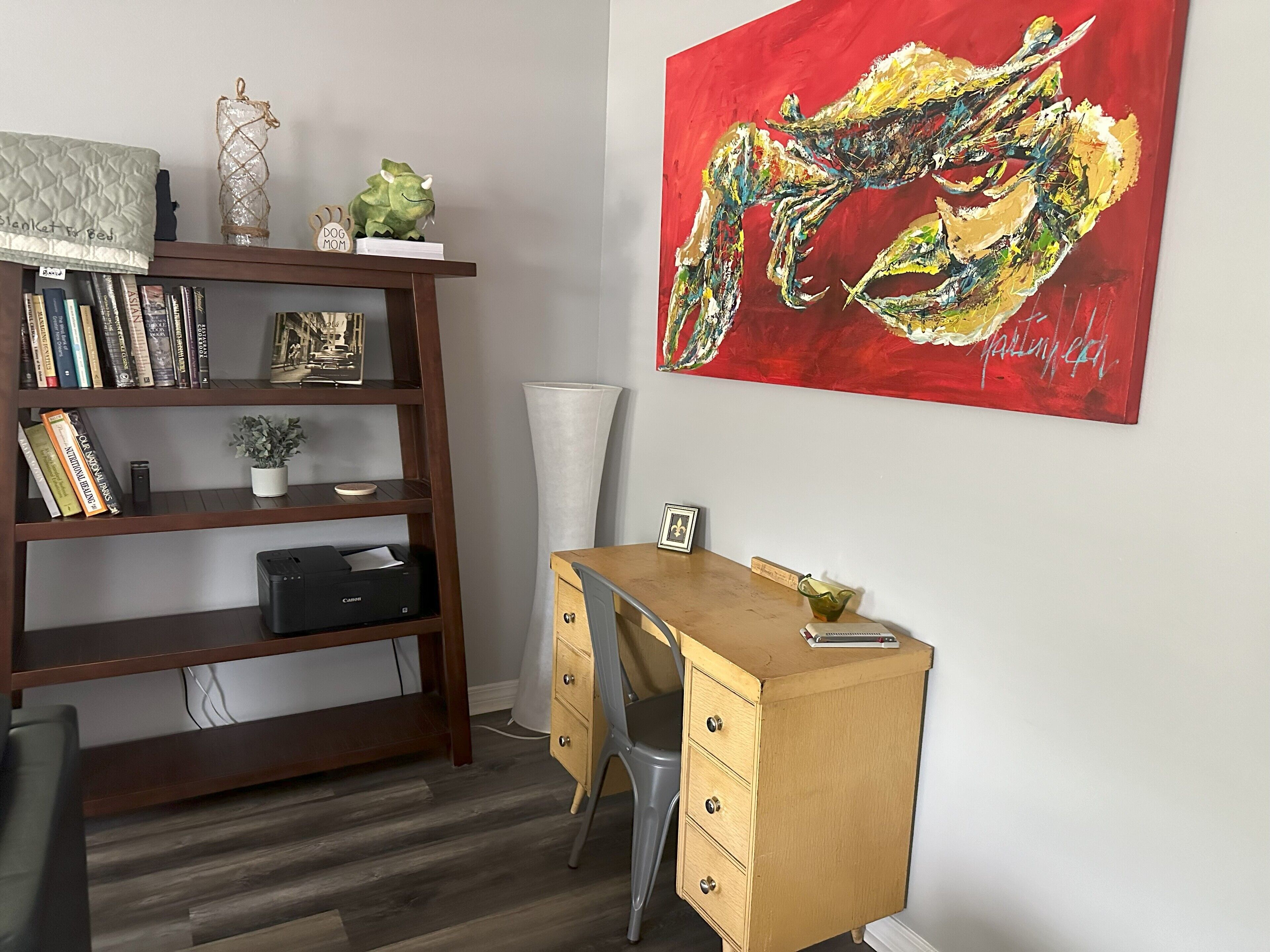 A room with a wooden desk, a bookshelf, and a large abstract painting.