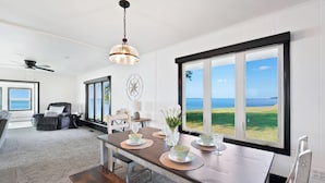 A dining area with a view of the ocean, a ceiling fan, and a dining table set with plates and glasses.