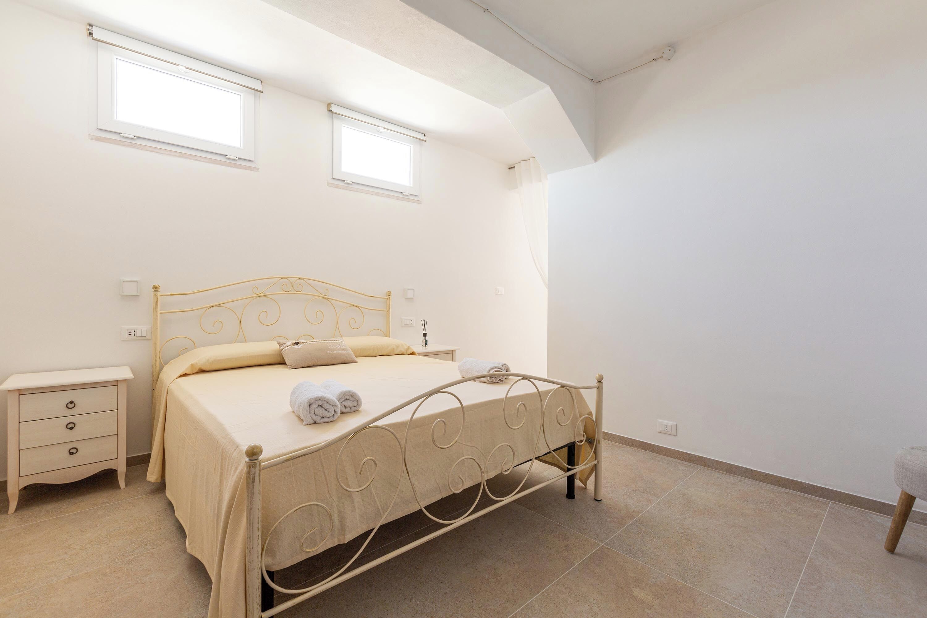 A bedroom with a bed, bedside tables, and two windows.