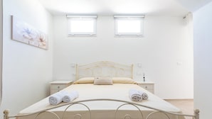 A bedroom with a bed, two bedside tables, a wall-mounted artwork, and two windows.