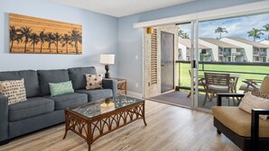 Un salon avec un canapé, une table basse en verre et une vue sur un balcon aménagé avec du mobilier d’extérieur.