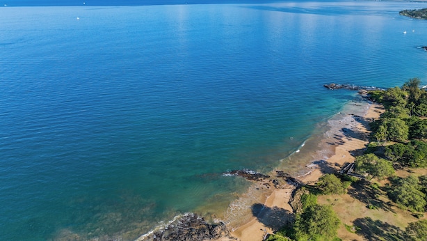 Un paysage côtier caractérisé par une eau d’un bleu limpide, une plage de sable et des affleurements rocheux.