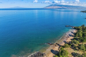 A coastal landscape with clear blue waters, a sandy beach, and rocky outcrops. - Charming Condo Steps Away From Beach (Kihei)