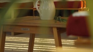 A white pitcher on a wooden table with a label, sunlight casting shadows on the floor.