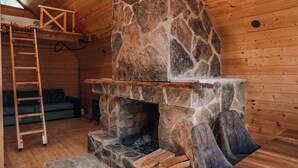 En stuga med träpanel på insidan, en steneldstad, en trästege och en soffa.