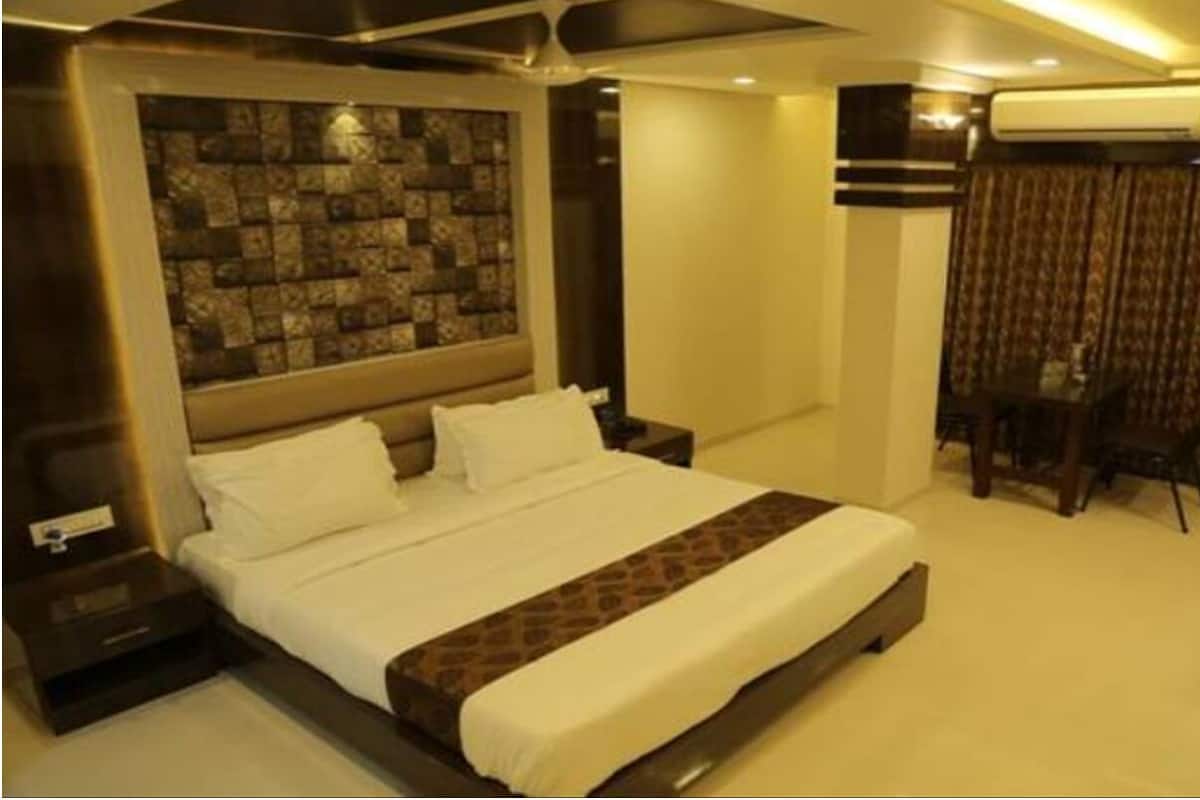 A hotel room with a large bed, a stone-patterned wall, an air conditioning unit, and a patterned curtain.