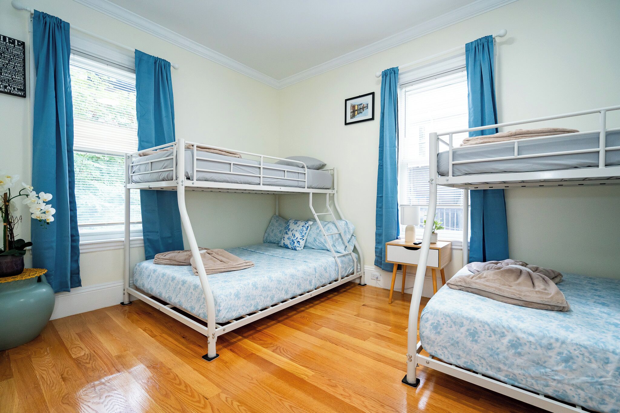 Une chambre avec deux lits superposés, un plancher en bois, un petit bureau et une fenêtre avec des rideaux.