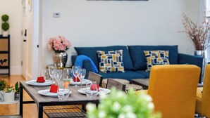 Un comedor con una mesa dispuesta para seis personas, un sofá azul con cojines estampados y un cuadro en la pared.