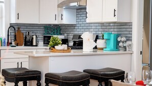 Una cocina moderna con armarios blancos, salpicadero gris y una isla central con taburetes.