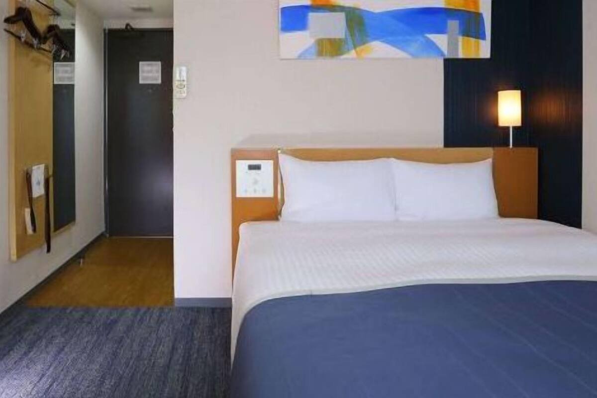 A hotel room with a bed, a desk, a television, and a painting on the wall.