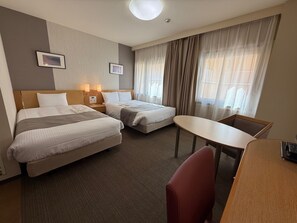 A hotel room with two beds, a desk, and a chair. There are two bedside tables with lamps, a window with curtains, and a wall-mounted picture. - HOTEL HOKKE CLUB OITA (Oita)