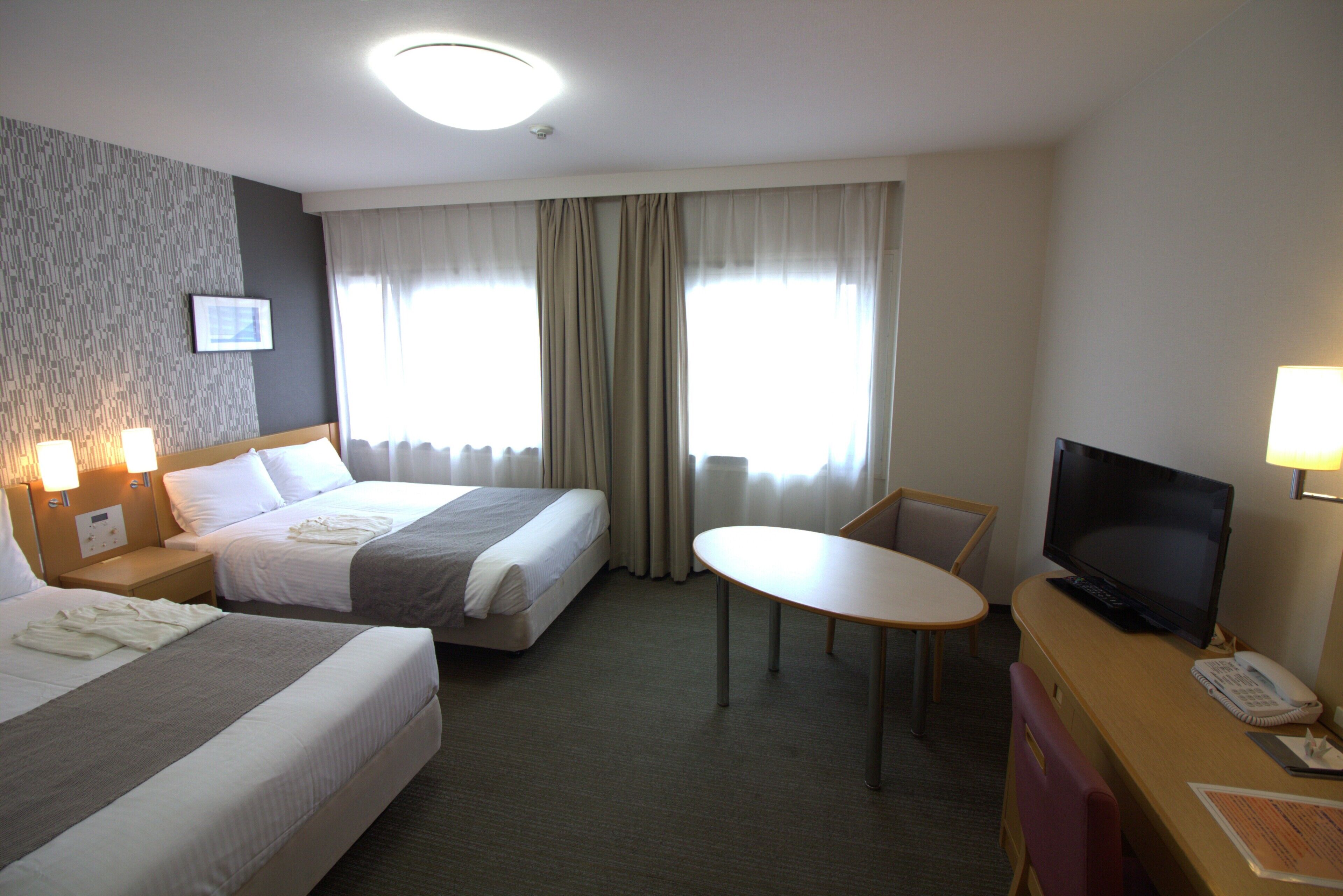 A hotel room with two beds, a desk with a television, and a small table.