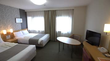 A hotel room with two beds, a desk with a television, and a small table.