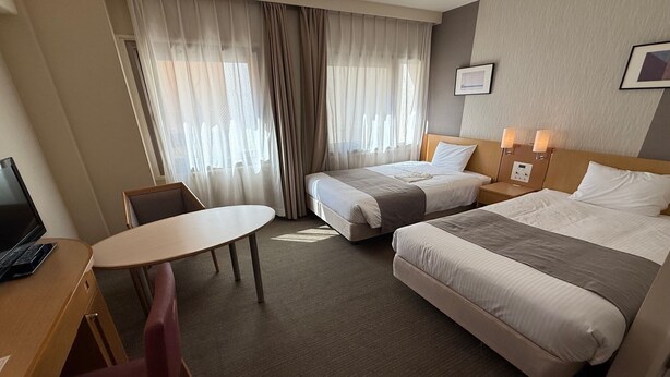 Hotellihuone, jossa on kaksi sänkyä, työpöytä, tuoli ja pieni pöytä.
