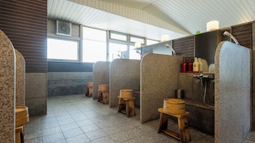 Baño público con cabinas individuales, taburetes de madera y zona de ducha.