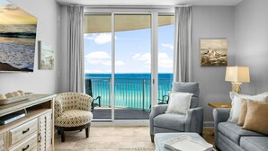 Una sala de estar moderna con un balcón que da a un mar turquesa, con un sofá, un sillón y una mesa de centro.
