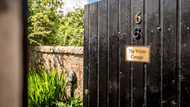 Una reja metálica negra con un cartel que dice 'The Whins Cottage'.