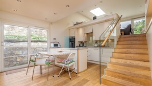 Una cocina moderna con una isla central, un comedor con dos sillas y una escalera que sube a un nivel superior.