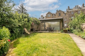 A house with a large garage door, a patio with a table and chairs, and a well-maintained garden. - The Whins Cottage | St Andrews (St Andrews)