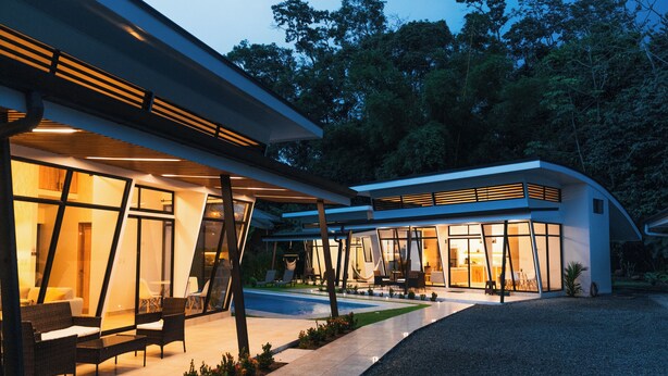 Una casa moderna con amplios ventanales, mobiliario exterior y un jardín cuidado.