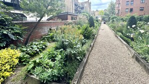 Un étroit sentier de gravier bordé d’une végétation luxuriante et de bâtiments en briques.