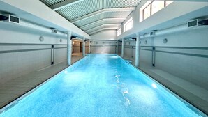 Une grande piscine intérieure dotée d’un haut plafond et de fenêtres de toit.