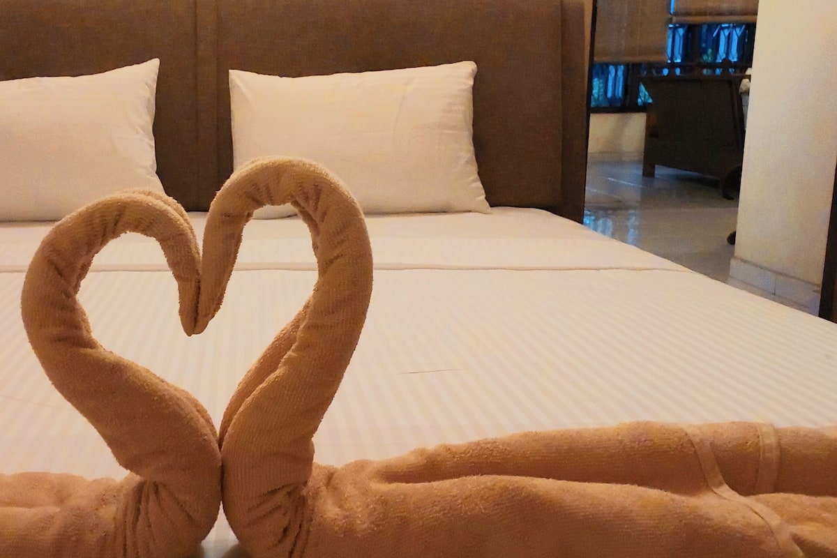Une chambre d’hôtel avec un lit, deux oreillers et une serviette pliée en forme de cœur posée sur le lit.