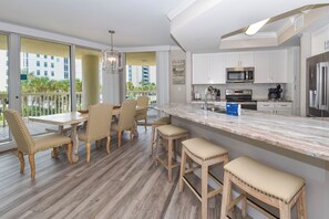 A modern kitchen with a marble countertop, stainless steel appliances, and a dining area with wooden chairs and a table.