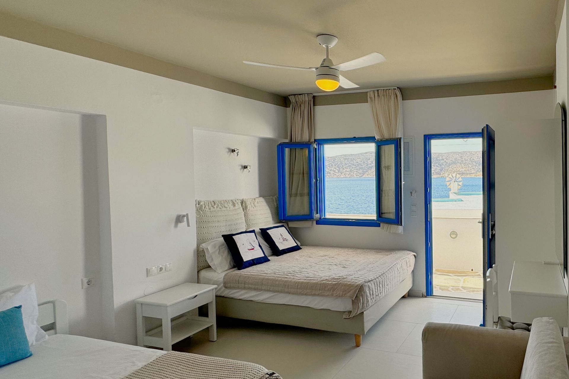 A bedroom with a bed, bedside table, and a view of the sea through a window.