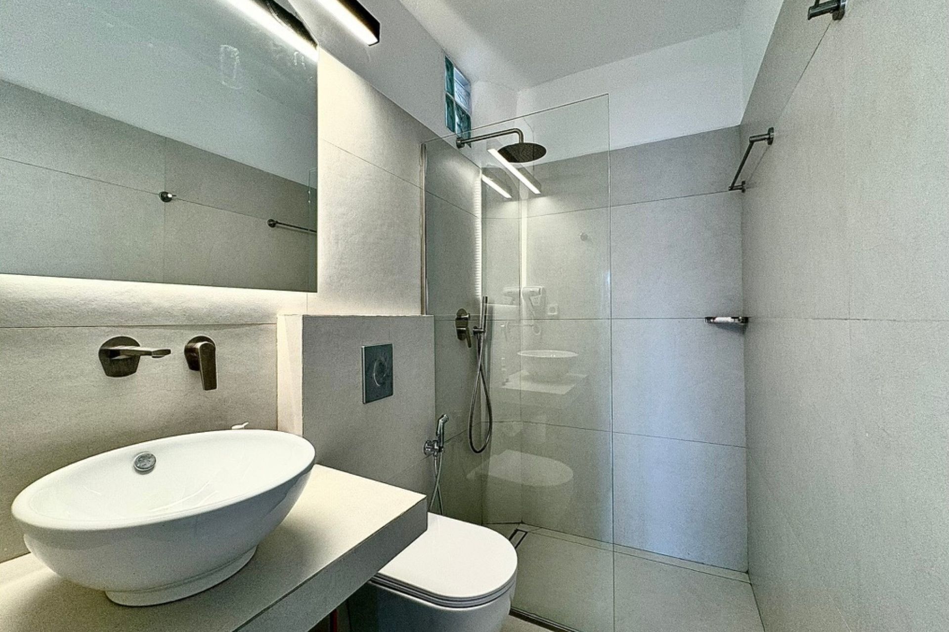 Un baño moderno con un lavamanos grande blanco, un inodoro y una zona de ducha con mampara de vidrio.