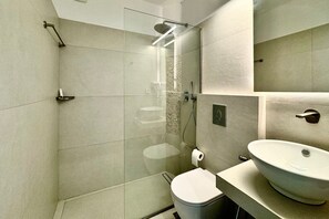 A modern bathroom with a glass-enclosed shower, a white toilet, and a large sink. - Eleni On The Beach (Amorgos)