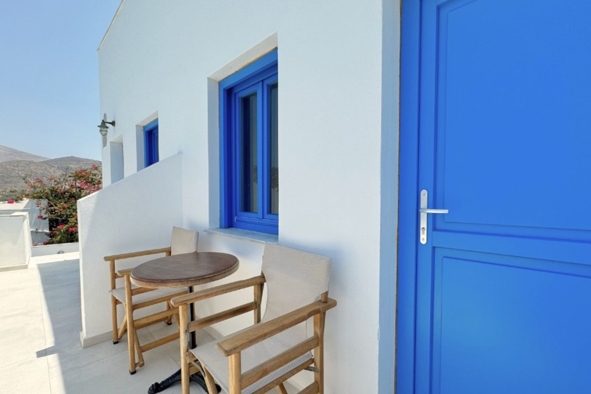 Un bâtiment blanc agrémenté de touches de bleu, une table ronde entourée de chaises et une porte bleue.