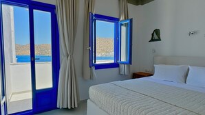 Ein Schlafzimmer mit Bett, Nachttisch, einem Fenster mit Vorhängen und Blick auf das Meer.