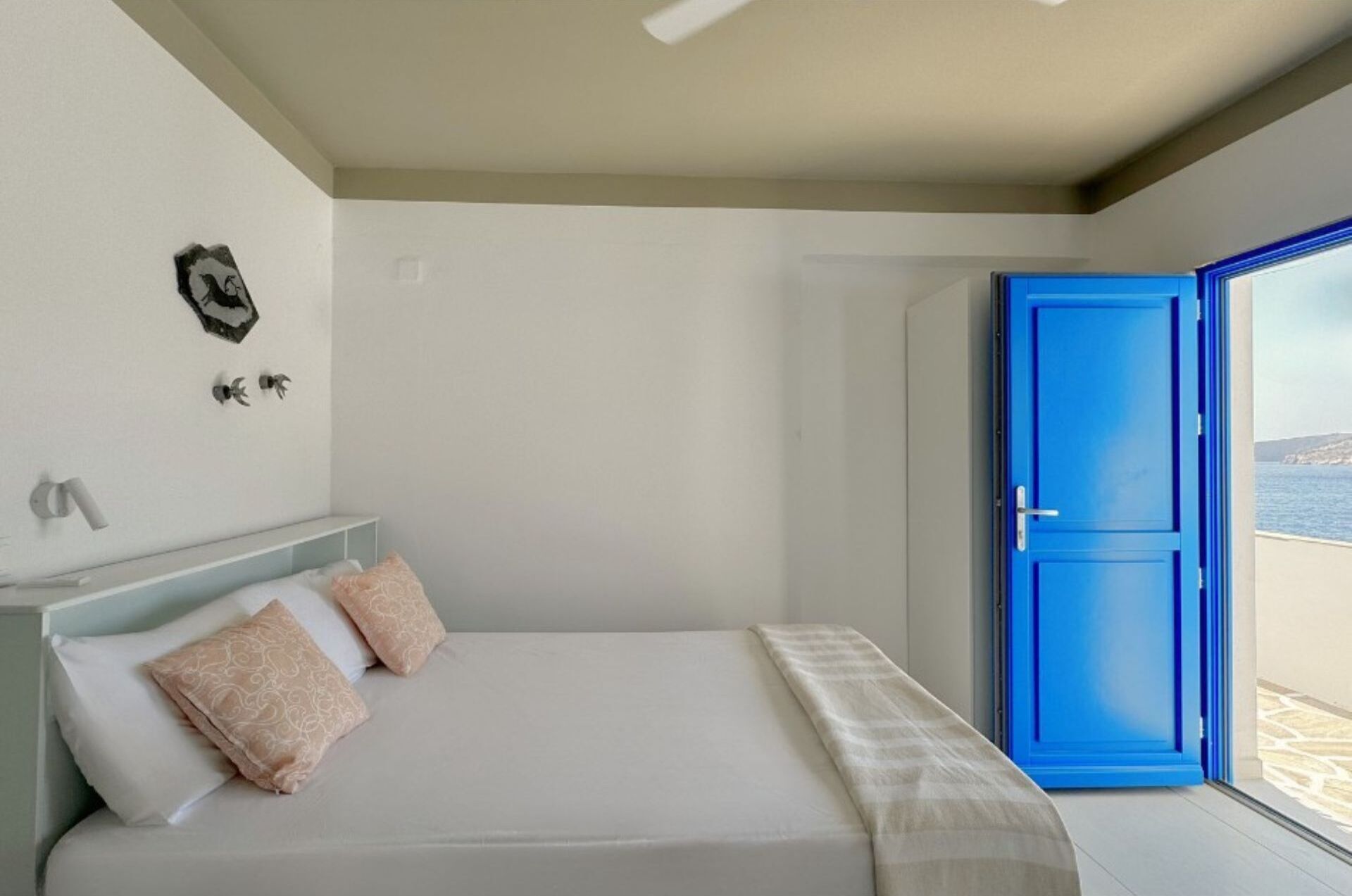 A bedroom with a bed, a blue door, and a view of the sea.