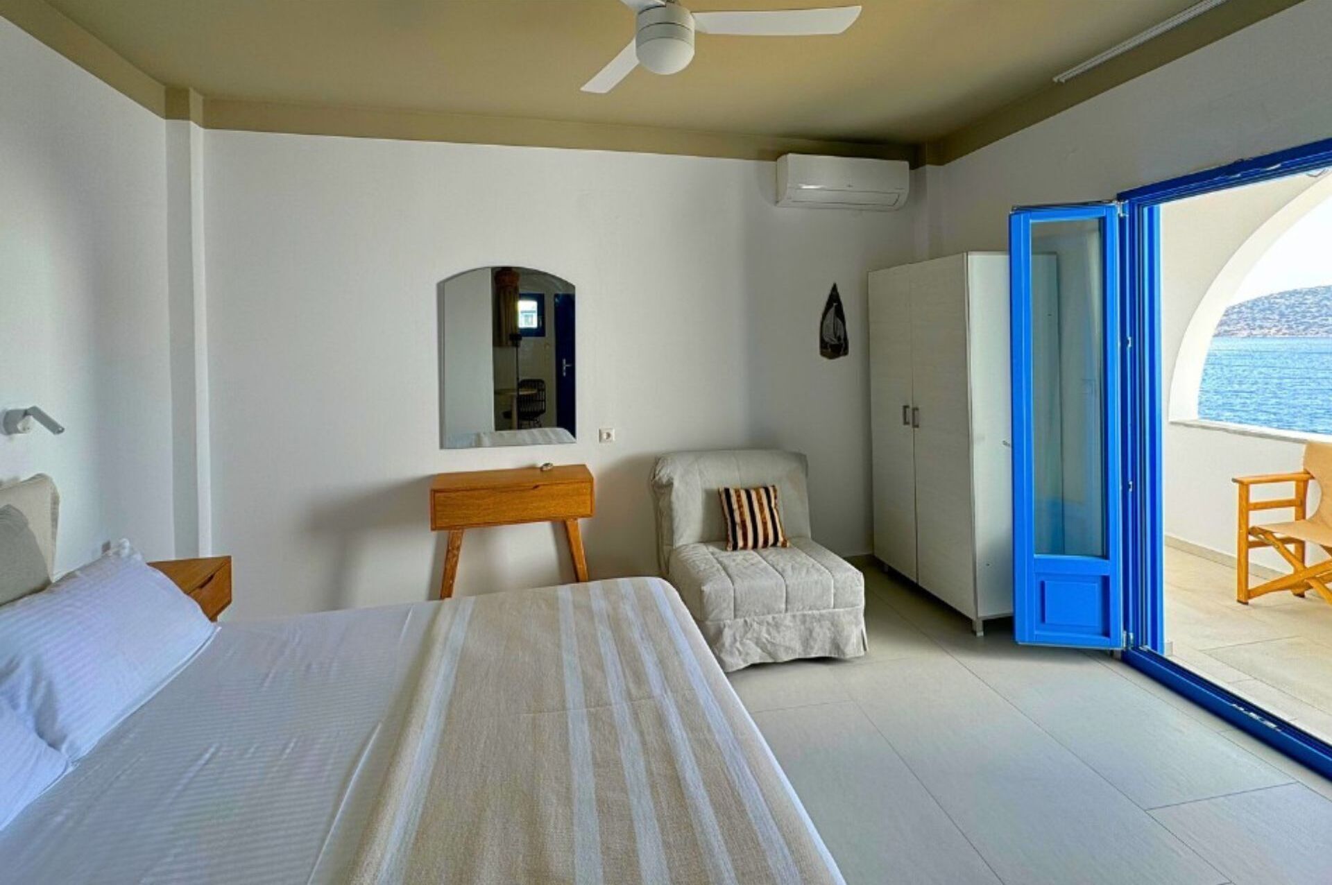Un dormitorio con cama, una silla, un escritorio, un armario y un balcón con vista al mar.