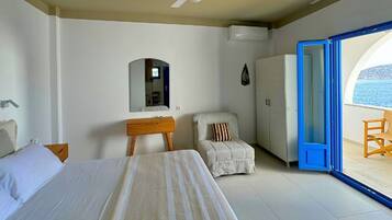 Un dormitorio con cama, una silla, un escritorio, un armario y un balcón con vista al mar.